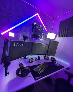 a computer desk with two monitors and headphones on it, in front of a purple light