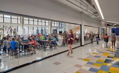 people are sitting at tables and walking around in the cafeteria with glass walls on both sides