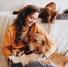 a woman is sitting on the couch with two dogs and petting her dog's head