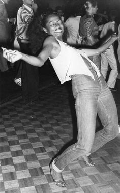 a black and white photo of a woman dancing on the dance floor with other people in the background