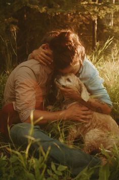 a man hugging his dog while sitting in the grass with sun shining through trees behind him