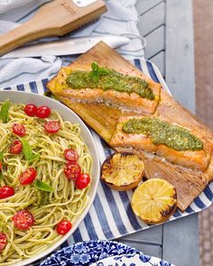 a plate of pasta with pesto on it next to a platter of fish