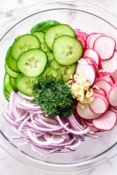 sliced cucumbers, onions and other vegetables in a glass bowl on a marble surface