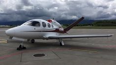 a small white airplane sitting on top of an airport tarmac under cloudy skies and clouds