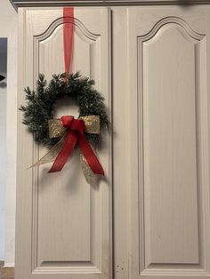 a door with a wreath hanging on it's side and a red ribbon tied to the front