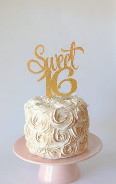 a white cake topped with a gold sweet 16 topper on a pink plate next to a white wall