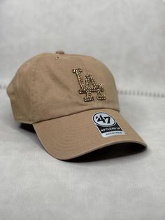 This is a khaki tonal LA Dodgers 47 clean up women's adjustable hat that is hand embellished with  translucent gold Swarovski crystals on the front logo to match. This hat features over 150+ Swarovski crystals.  - 100% Cotton - Matching fabric strap & buckle  - One Size Fits All - Raised Embroidered Logo - 150+ Swarovski translucent gold crystals individually placed by hand - Ready to ship in 1 week from San Diego, CA Bling Dodgers Hat, Bling Hat, Gold Crystals, Fabric Strap, Adjustable Hat, Trucker Cap, Clean Up, Caps Hats, San Diego