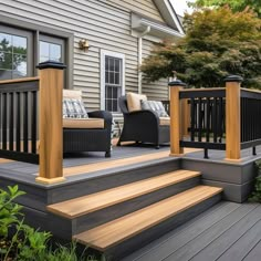 an outdoor deck with chairs and steps leading up to the front door, next to a house