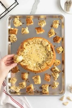 someone is holding a piece of bread with cheese on it in front of a baking sheet