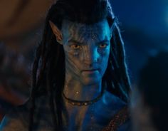 a man with dreadlocks and blue makeup looks at the camera while standing in front of other people