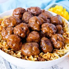 meatballs and noodles in a white bowl on a blue towel next to yellow flowers