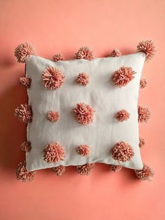 a pink and white pillow with pom - poms on the front, against a peach background