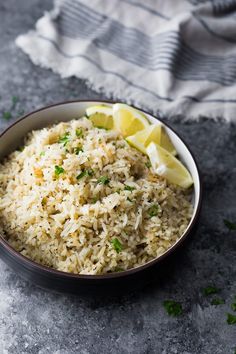 a bowl filled with rice and lemon wedges on top of a gray tablecloth