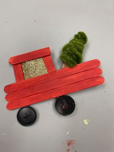 a red wooden toy train with a green plant in the front and two black knobs on each side