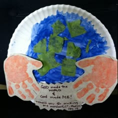 a paper plate with two hands and green leaves on it that says god made the world