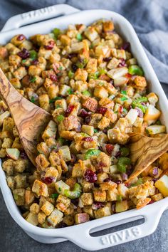 a white casserole dish filled with stuffing and cranberries, topped with a wooden spoon