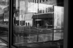 the reflection of people walking on the sidewalk in front of a building with large windows