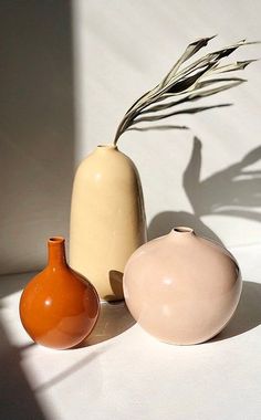 three vases sitting next to each other on a white tablecloth with shadows from the wall behind them