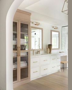 a white bathroom with wooden floors and cabinets in the corner, along with large mirrors