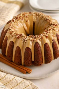 a bundt cake with icing and nuts on a plate next to cinnamon sticks