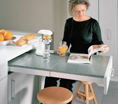 a woman sitting at a kitchen counter reading a book and drinking orange juice in front of her