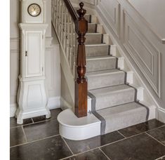 there is a clock on the wall next to the stairs in this house with tile flooring