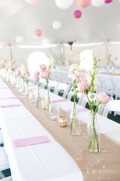 there are many vases with flowers in them on the long table at this wedding reception