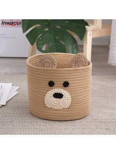 a brown bear shaped basket sitting on top of a floor next to a green plant