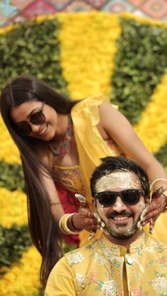 a man is getting his hair cut by a woman in front of flowers and bushes