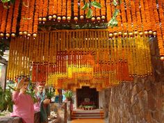 an outdoor shrine with orange beads hanging from it's ceiling and two women standing under the altar