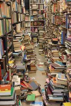 a large amount of books are stacked up on the floor in a room full of shelves