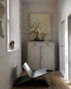 a room with white walls and wood flooring has a vase on top of the cabinet