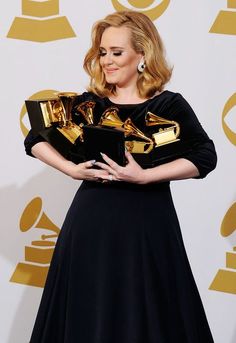 a woman in a black dress holding two golden trophies and an award for outstanding performance