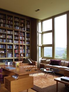 a living room filled with lots of books and furniture next to a window covered in windows