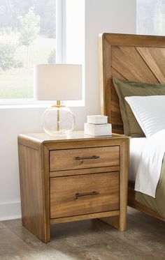 a nightstand with two drawers and a lamp on top of it next to a bed