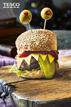 a cheeseburger with pickles and olives on a wooden table next to a spider