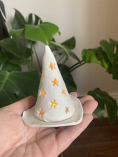 a hand holding a small white cone with orange stars on it and a potted plant in the background