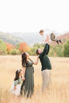 an adult holding a baby up in the air while standing next to two young children