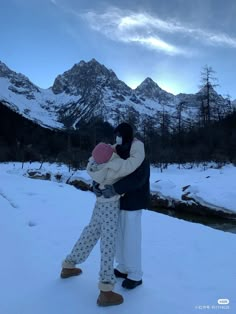 a man and woman hugging in the snow with mountains in the backgrouds