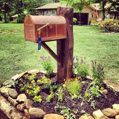 a mailbox sitting on top of a wooden post in the middle of a flower bed