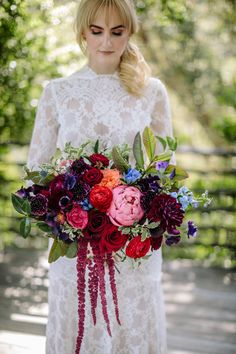 a woman in a white dress holding a bouquet of red, purple and green flowers