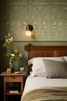 a bedroom with green wallpaper and white bedding, two vases filled with flowers