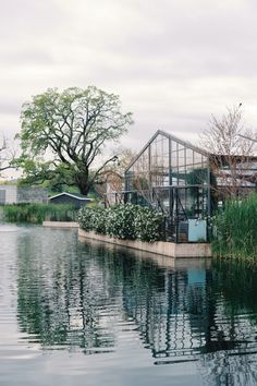 there is a house sitting on the water's edge next to some trees and bushes