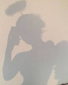 a shadow of a woman holding a cell phone to her ear and standing in front of a wall