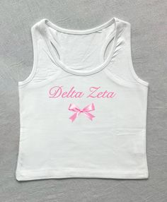 a white tank top with pink lettering and a bow on the front that says delta zera