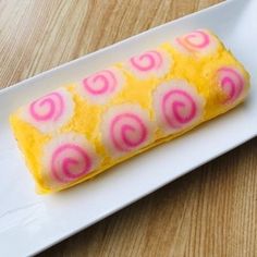 a white plate topped with yellow and pink cake on top of a wooden table next to a fork