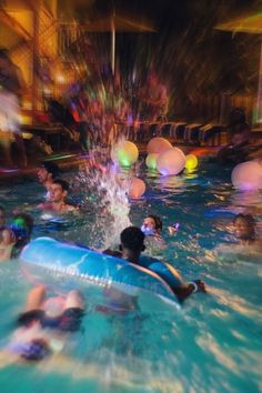 people are playing in the pool at night with floats and water balloons floating around them