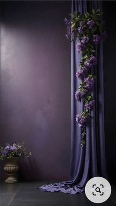 a purple curtain with flowers on it in front of a wall and a potted plant