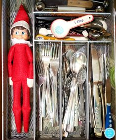 an elf is sitting in a drawer with silverware and utensils on it