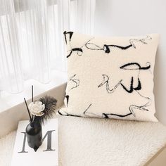 a black and white pillow sitting on top of a bed next to a vase with flowers